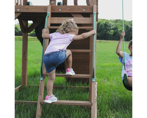 Mädchen klettert auf eine Holzleiter eines Kinderspielhauses im Freien