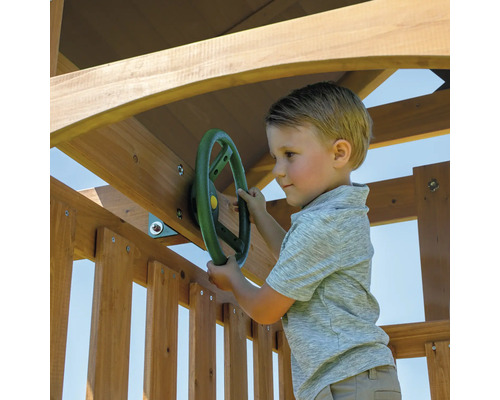Junge spielt mit einem Lenkrad an einem hölzernen Spielturm