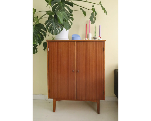 Schrank aus Holz mit zwei Türen und vier Füßen, dekoriert mit einer Zimmerpflanze und Kerzen