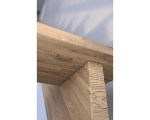 Detailansicht eines Holztisches, die die Maserung und die Befestigung der Tischbeine zeigt.