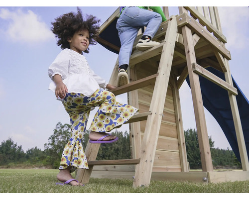 Kinder klettern auf ein hölzernes Spielhaus mit Rutsche im Garten.