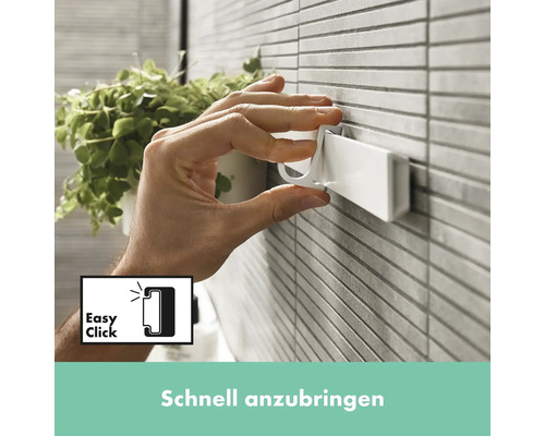 Eine Hand befestigt einen weißen Haken an einer Wandhalterung im Badezimmer.