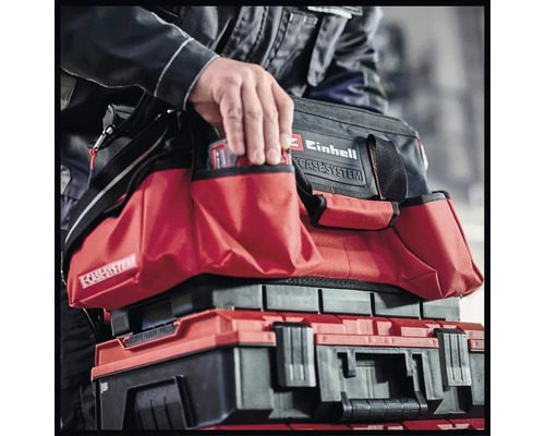 Ein Mann greift in eine Einhell Werkzeugtasche, die auf einem Einhell Werkzeugkoffer steht.