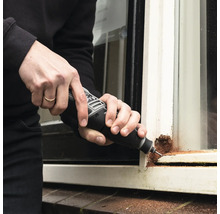 Eine Person repariert einen Fensterrahmen mit einem Multifunktionswerkzeug.