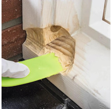 Eine Hand mit Handschuh verwendet einen Spachtel, um Holzspachtel aufzutragen.