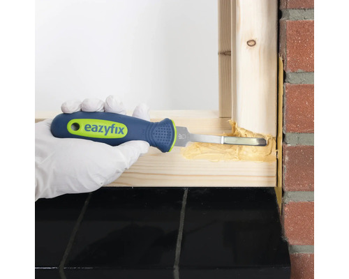 Eine Person dichtet mit einem Fugenkratzer einen Fensterrahmen ab.