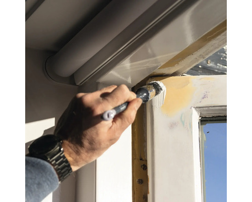 Eine Person streicht mit einem Pinsel einen Fensterrahmen.