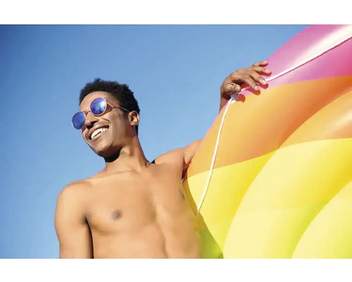 Mann mit Sonnenbrille und aufblasbarem Schwimmreifen vor blauem Himmel