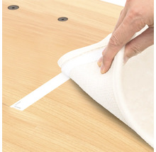 Eine Person befestigt einen Teppich mit einem Klebestreifen auf einem Holzboden.