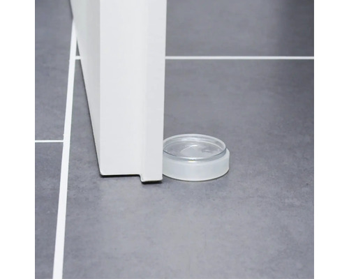 Transparenter Türstopper aus Kunststoff am Boden neben einer Tür.