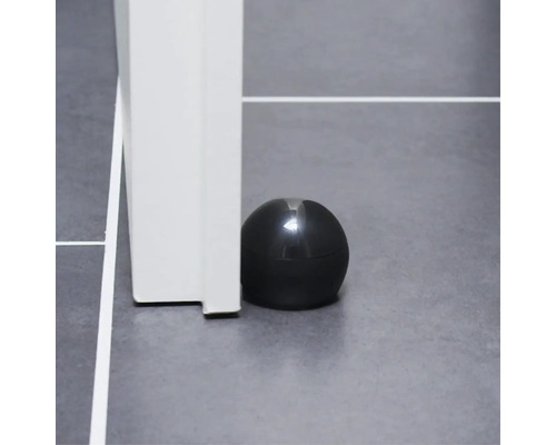 Schwarzer Türstopper neben einem weißen Türrahmen auf einem grauen Boden