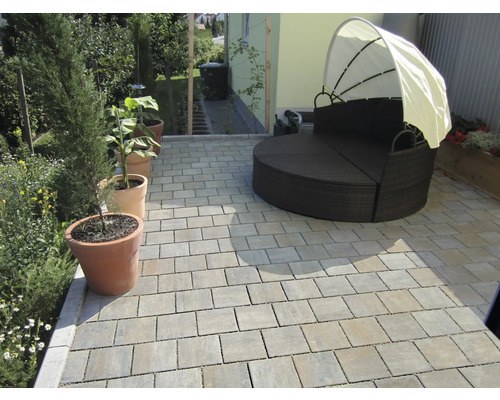 Terrasse mit Pflastersteinen und runder Gartenliege mit Sonnenschutz