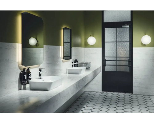 Badezimmer mit Waschbecken, Spiegel, Leuchten und Tür mit Glaseinsatz.