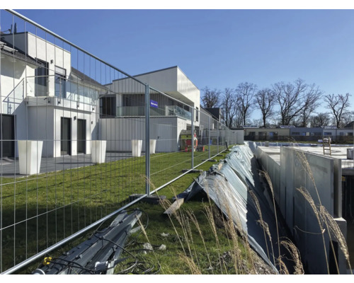 Baustelle mit Bauzaun vor modernen Häusern.