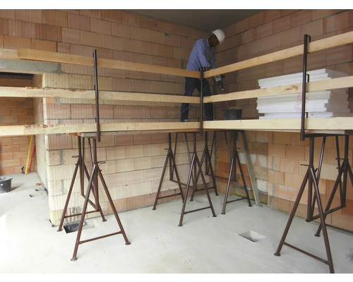 Baustellenszene mit Maurer auf Arbeitsbühne vor einer Ziegelwand