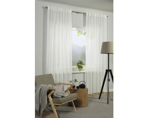 Wohnzimmer mit weißen, transparenten Gardinen vor einem Fenster, Sessel, Beistelltisch und Stehlampe