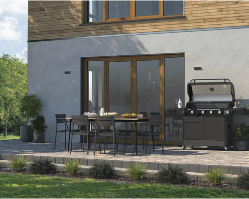 Terrasse mit Grill, Tisch und Stühlen vor einem Haus.