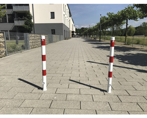 Zwei rot-weiss gestreifte Absperrpfosten auf einem gepflasterten Weg.