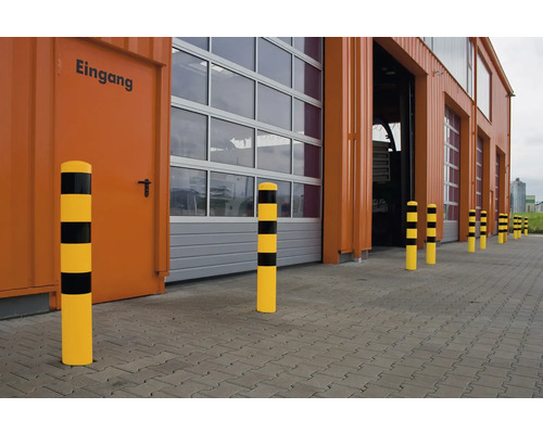 Gelb-schwarze Anfahrschutzpfosten vor einem Industriebau mit Toren und Eingangstür