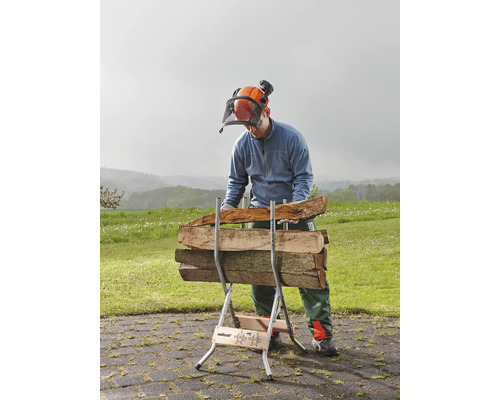 Ein Mann mit Schutzhelm und Visier arbeitet mit einem Holzspalter, auf dem Holzscheite liegen.