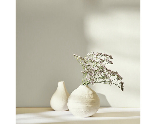 Zwei weiße Vasen, eine mit Trockenblumen, auf einem hellen Untergrund.