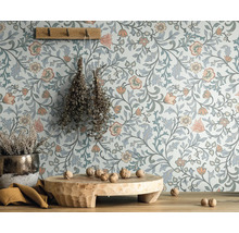 Szene mit blumiger Tapete, Holzhocker, Topfpflanze und Wandhaken mit Kräutern