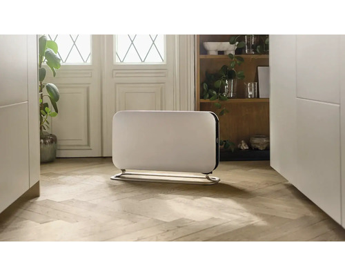 Weißer Heizkörper mit Fuß auf einem Holzboden in einem hellen Raum.