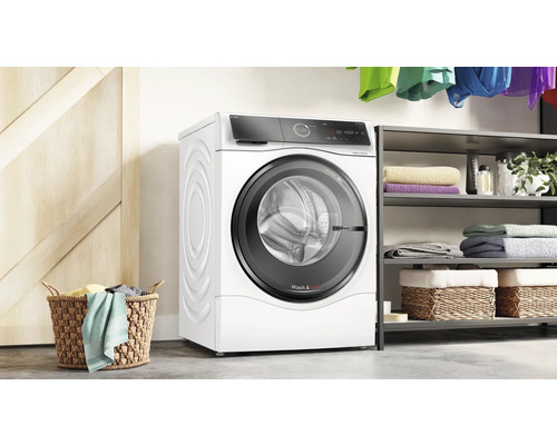 Weiße Bosch Waschmaschine in einem Waschraum neben einem Wäschekorb und einem Regal.