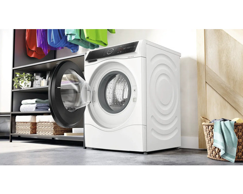 Weiße Waschmaschine mit offener Tür in einem Waschraum mit Regalen und Wäschekörben