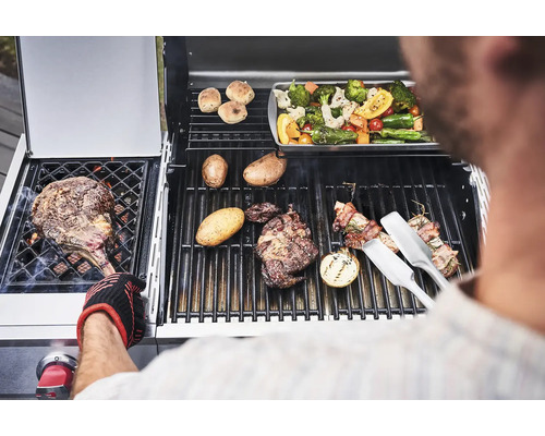 Mann grillt Steaks, Gemüse und Kartoffeln auf einem Gasgrill