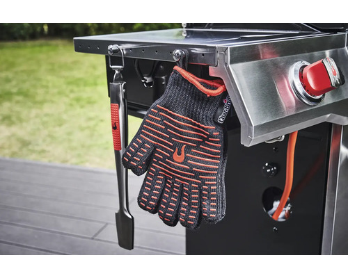 Grillhandschuh und Grillzange hängen an einem Grill.