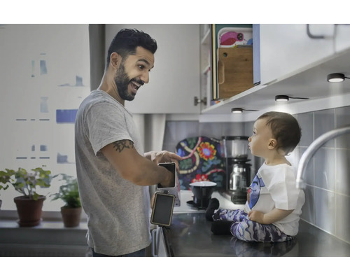 Vater zeigt Kind eine wiederaufladbare Leuchte in einer Küche mit Unterbaubeleuchtung.