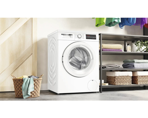 Freistehende Waschmaschine mit Wäschekorb und Regal im Hintergrund