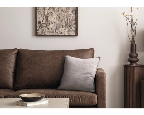 Wohnzimmer-Szene mit braunem Ledersofa, Dekokissen, Tisch, Dekoration und Kunstwerk