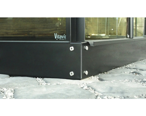 Detailansicht eines Gewächshausrahmens aus Metall mit Schrauben auf einem Steinboden. Vitavia Logo.