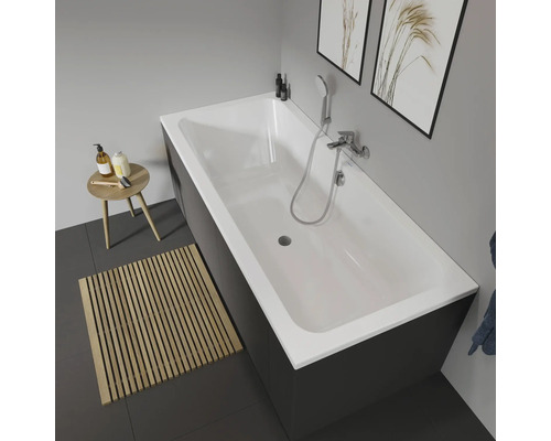 Szene eines Badezimmers mit einer rechteckigen Badewanne mit Armatur, einem Hocker und einer Holzmatte