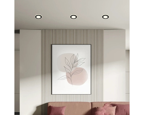 Ansicht eines Wohnzimmers mit Deckeneinbaustrahlern, Wandpaneelen, einem gerahmten Kunstdruck und einem Sofa.