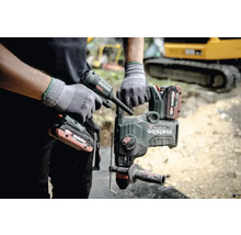 Ein Mann hält einen Metabo Bohrhammer und eine Kartuschenpistole in der Hand, im Hintergrund ist ein Bagger zu sehen