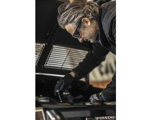 Ein Mann in Schutzbrille, der an einem Auto arbeitet.