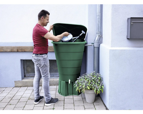 Mann befüllt eine Regentonne mit Gießkanne und Eimer.