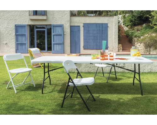 Szene im Freien mit einem weißen Gartentisch und passenden Stühlen auf einer Rasenfläche vor einem Haus.