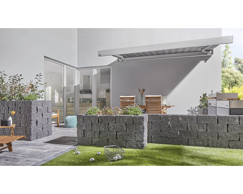 Außenbereich mit Steinmauern, Markise, Gartenmöbeln und Boulekugeln auf Rasen