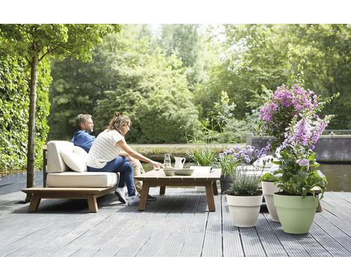 Entspannte Szene mit Gartenmöbeln, Tisch und bepflanzten Blumentöpfen auf einer Holzterrasse im Grünen.