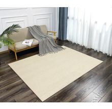 Ein Wohnzimmer mit einem hellen Teppich mit Fischgrätenmuster, einem Sofa, Vorhängen und einer Zimmerpflanze