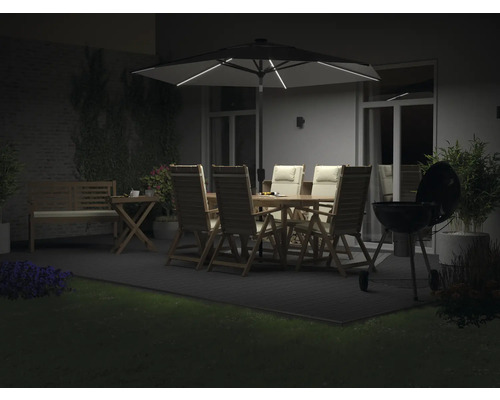 Beleuchtete Terrasse mit Gartentisch, Stühlen, Sonnenschirm und Grill
