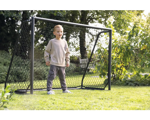 Ein Junge steht vor einem Fußballtor im Garten.