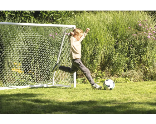 Junge schießt Fußball vor einem Fußballtor im Garten