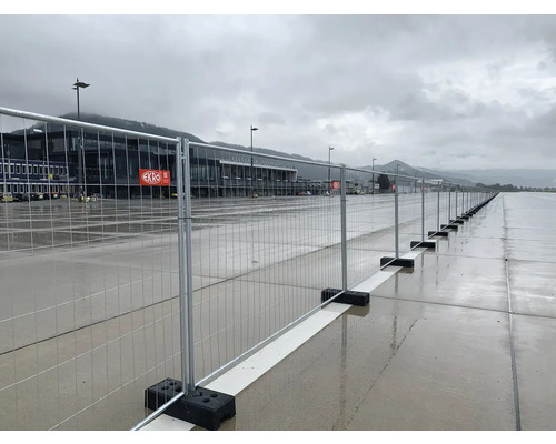 Bauzaun vor einem Flughafengebäude unter bewölktem Himmel