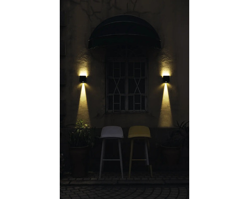 Außenansicht eines Gebäudes mit zwei Barstühlen unter einem Fenster mit zwei Wandleuchten.