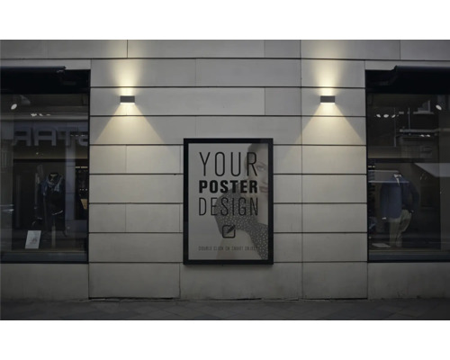 Ein gerahmtes Plakat hängt an einer Fassade zwischen zwei Schaufenstern mit Außenleuchten